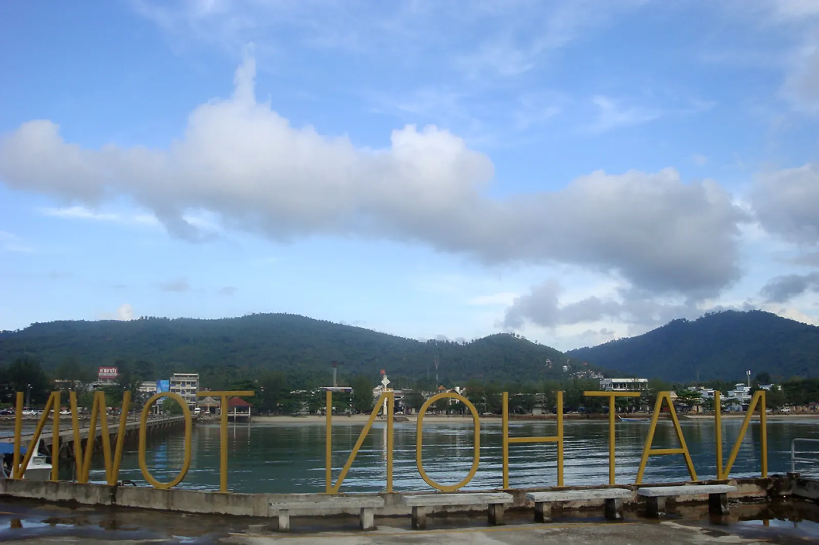 Nathon town on Koh Samui, seen from the old ferry pier, with fishing boats along the shore and green hills behind the town