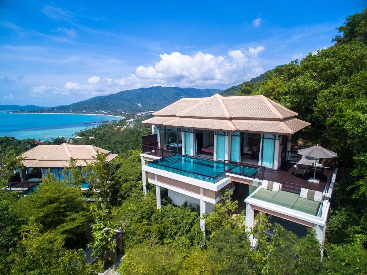 Banyan Tree Samui private pool villas aerial view — Thai-style pavilions with private infinity pools set into tropical hillside, Lamai Bay and the Gulf of Thailand stretching out below