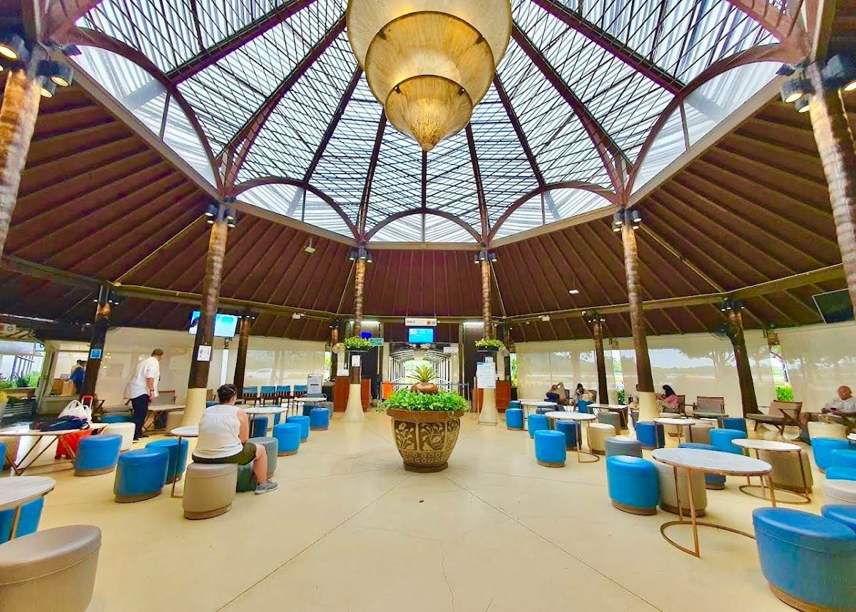 Interior of Samui Airport's distinctive round open-air terminal building, with its conical timber-and-thatch roof, tropical plants, and blue seating