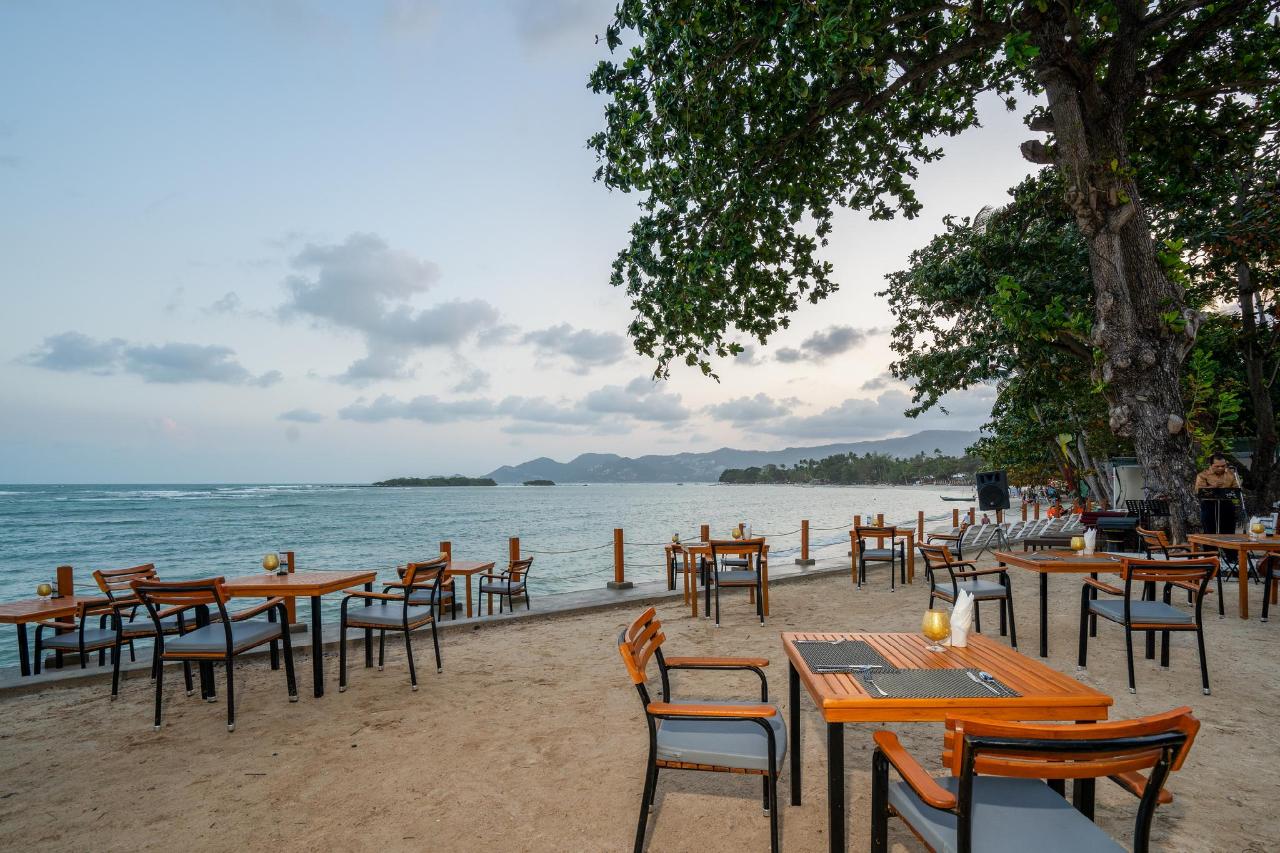 Sandy beach with palm trees and a green headland, in a photo on The Briza Beach Resort's Agoda gallery