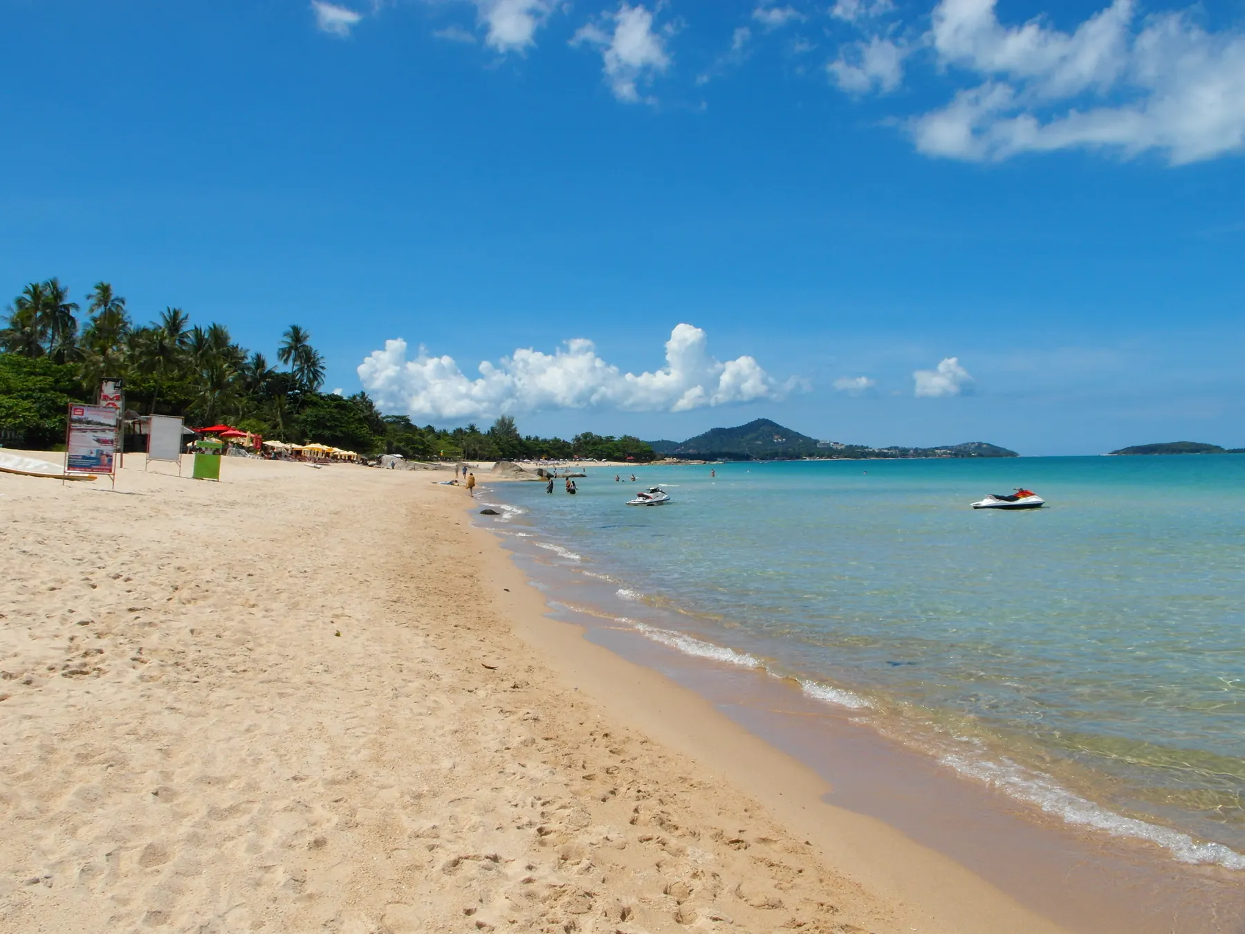 Chaweng Noi, the quieter south end of Chaweng. Chaweng Noi on Koh Samui, clear green water over a sandy bottom with swimmers and a line of palms